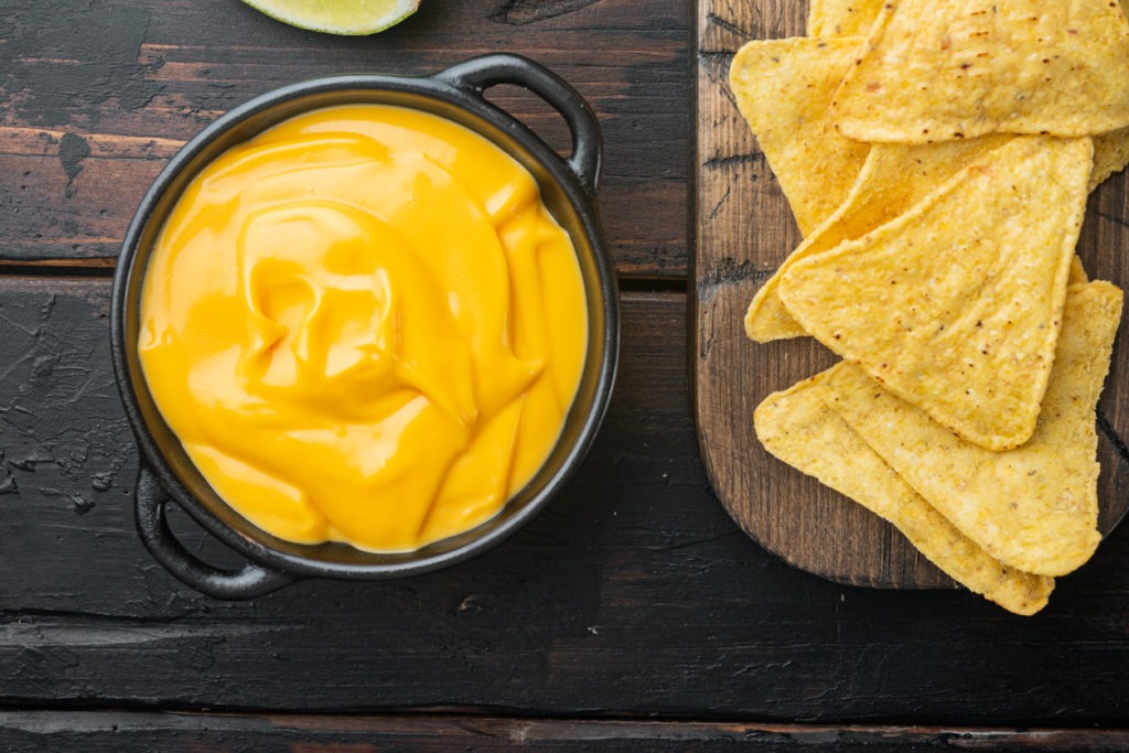 Tortilla chips with cheese dip, on old wooden table, top view or flat lay