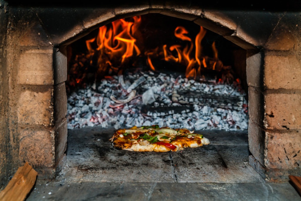 A pizza oven with burning charcoal and wood and a pizza being cooked