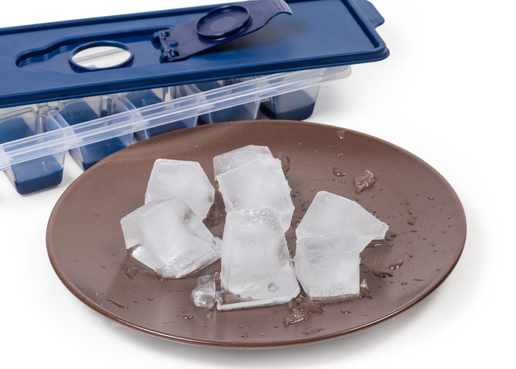 Ice cubes on dish against ice cube tray, close-up