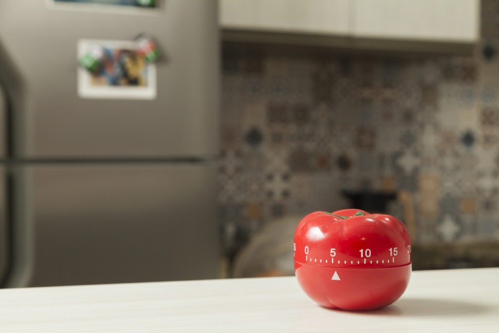 Red tomato-shaped kitchen timer with blurred kitchen in the background