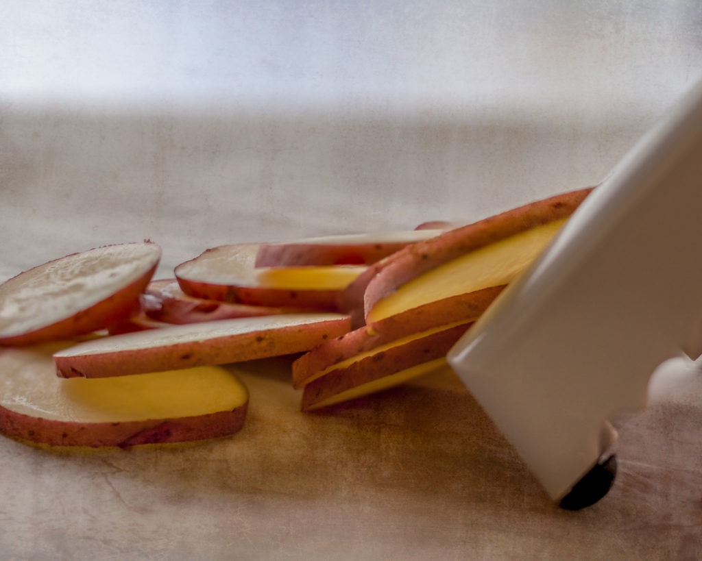  Slicing organic gold potatoes on a V-blade mandolin to prepare scalloped potatoes....