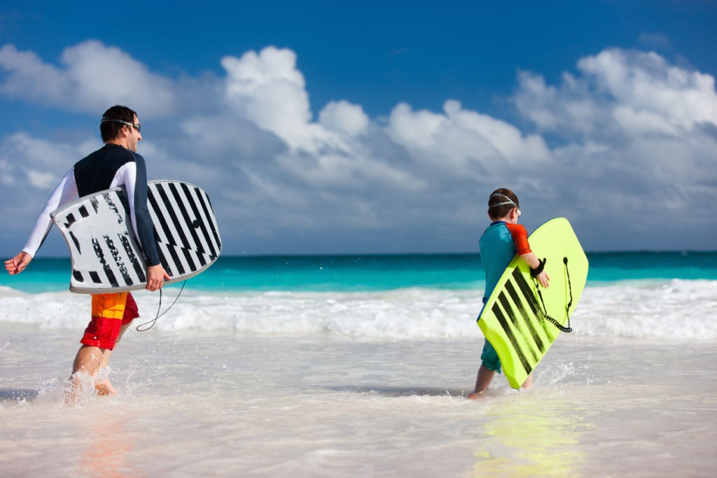 Father and son running towards the ocean with boogie boards