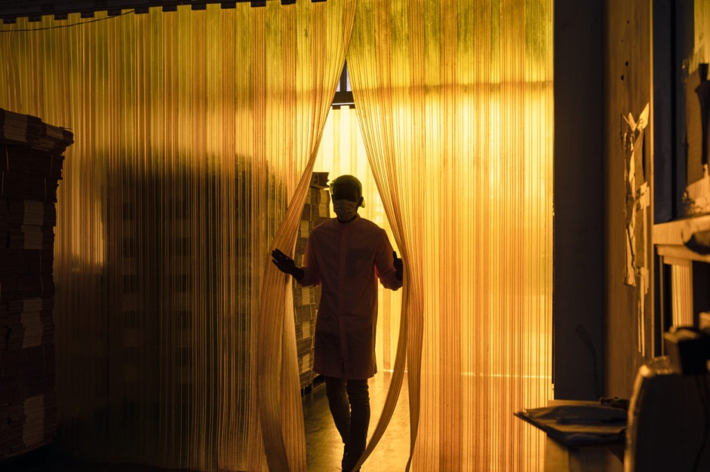 African male worker opening plastic curtain into cardboard package warehouse