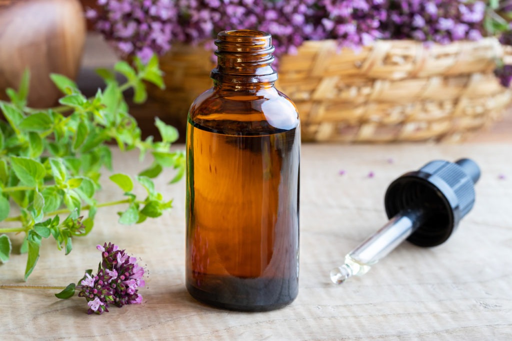 bottle of oregano oil with dropper and fresh oregano background