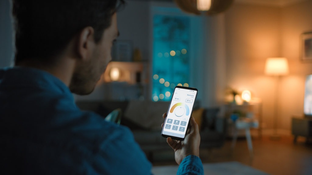 A man gives a voice command to a smart home application on his smartphone to change light temperature