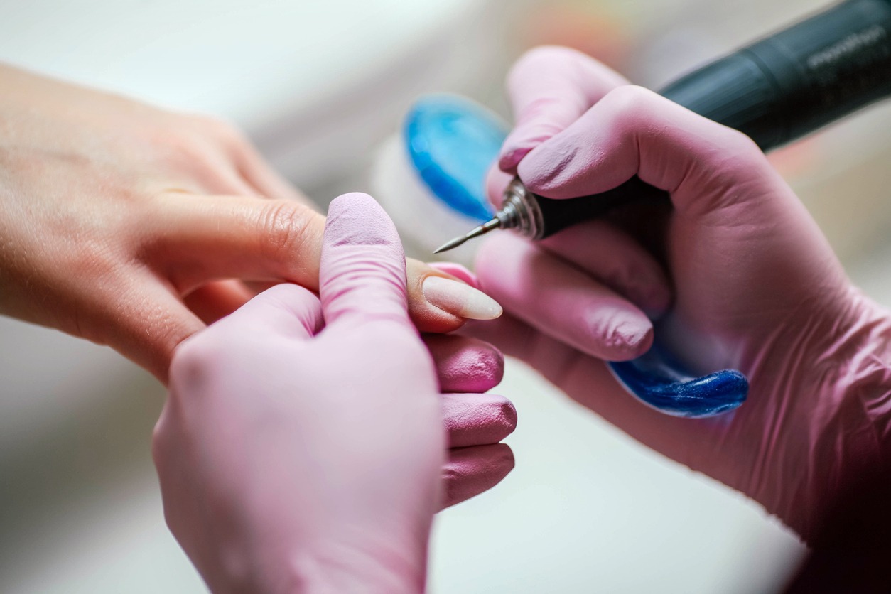 Woman uses electric nail file drill in beauty salon.