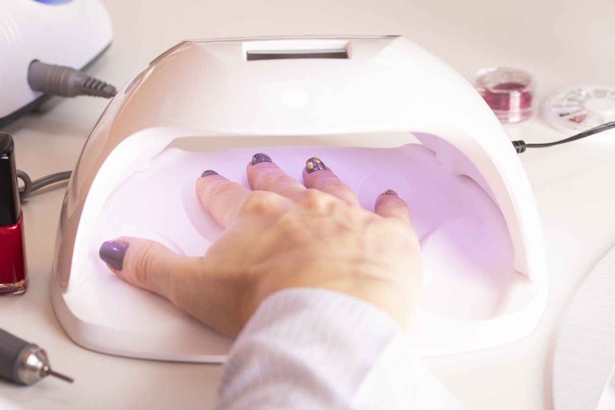 The hands of the girl in the UV lamp for nails on the manicure table
