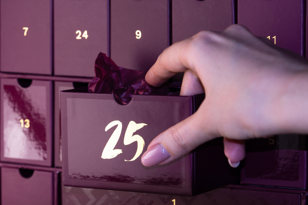 A woman's hand opens cell number 25 in the advent calendar. A gift wrapped inside a purple advent calendar. A Christmas gift