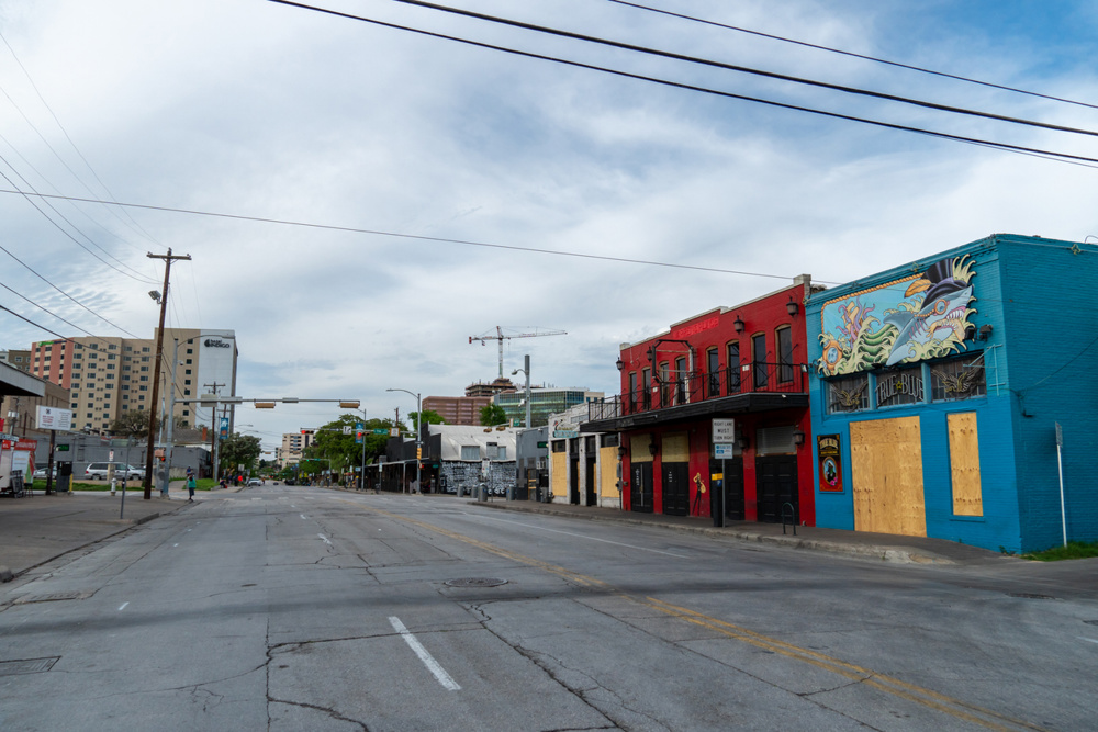 View of bars closed with playwood on Red River St from 6th Steet during the day
