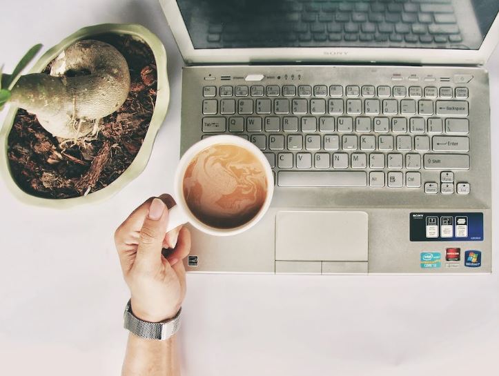 Person holding white mug on gray laptop computer
