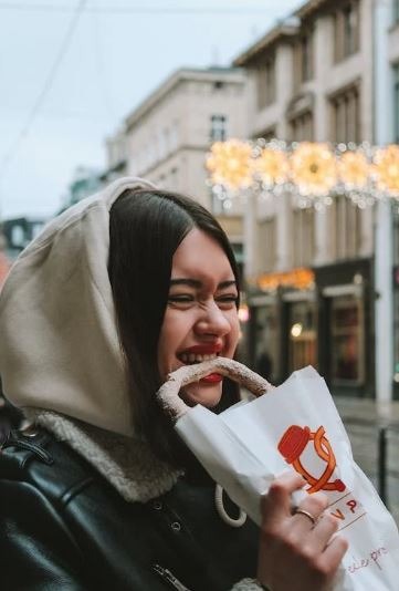 A woman in black leather jacket biting a pretzel.