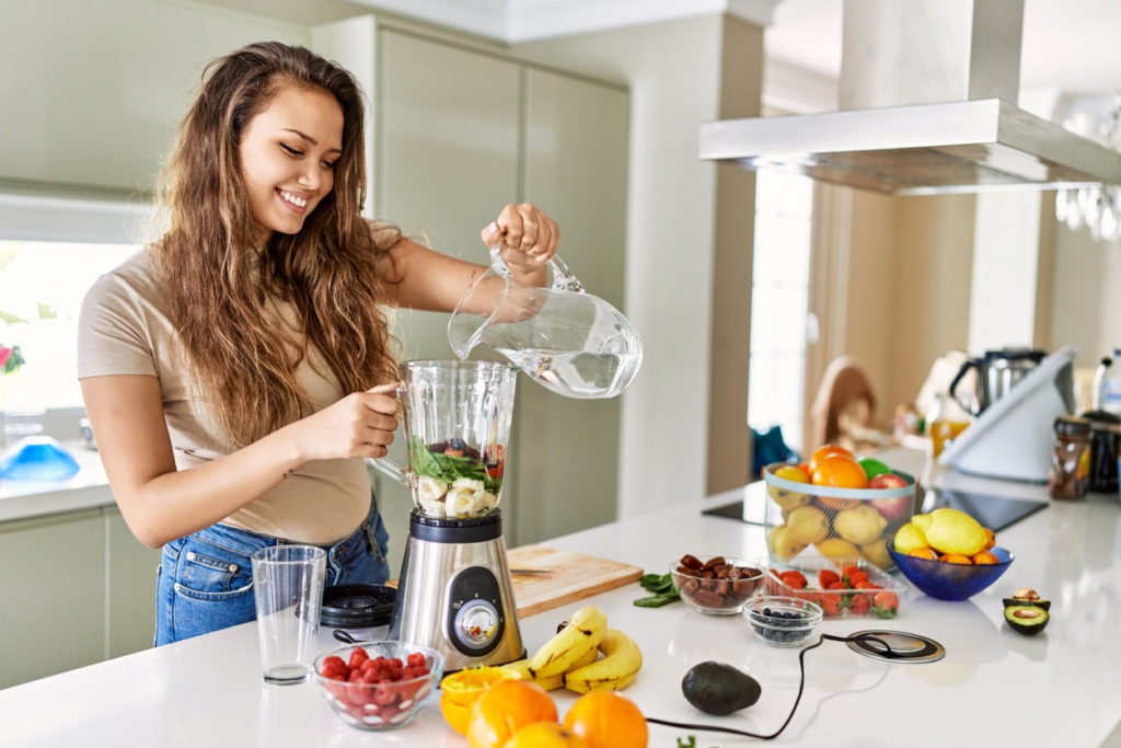 A woman putting ingredients in a plastic blender jar
