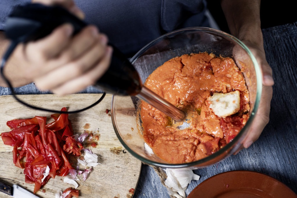 A man preparing a cold tomato soup using an immersion blender