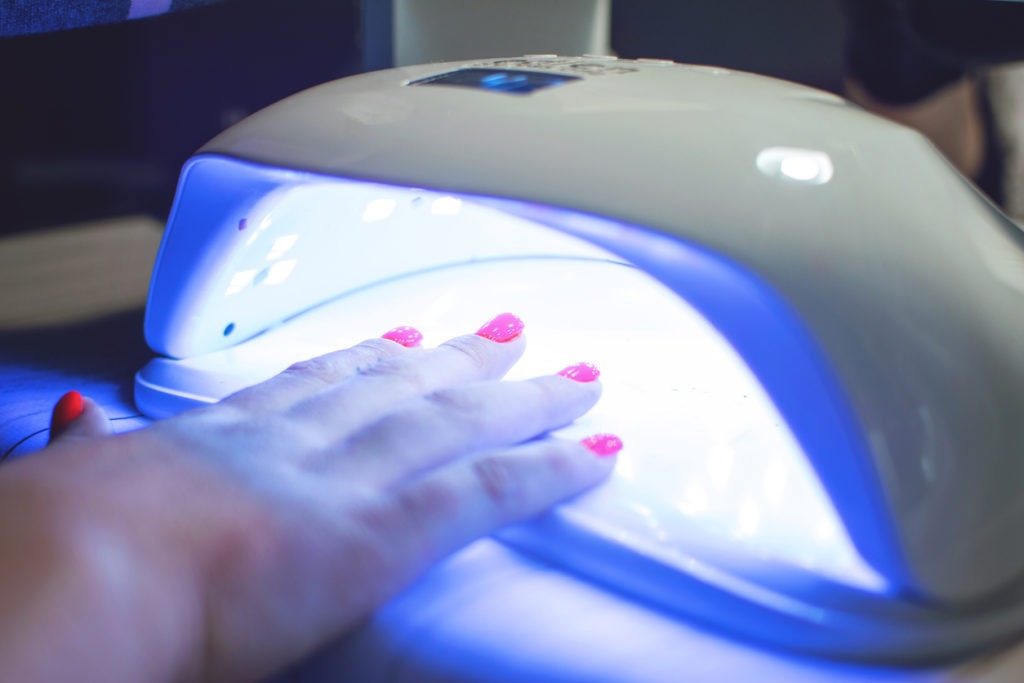 Female Hand with red nails in the lamp for manicure. Nail Lamp Dryer for Gel Nail Polish Curing Manicure Pedicure