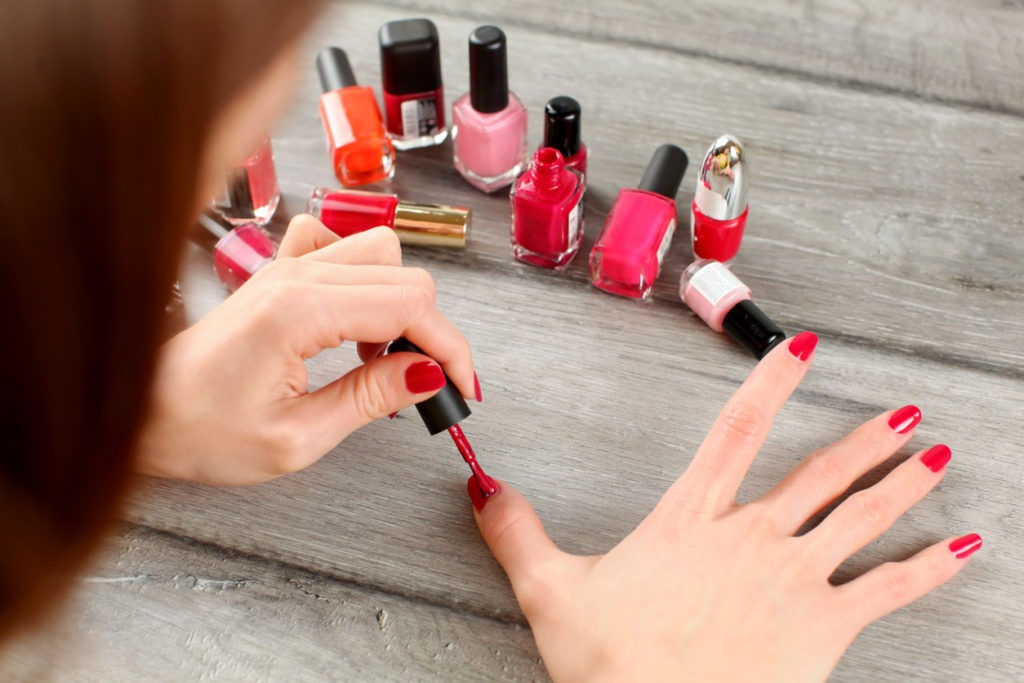 Top view on woman hands, applying red nail polish, with more bottles with varnish in background