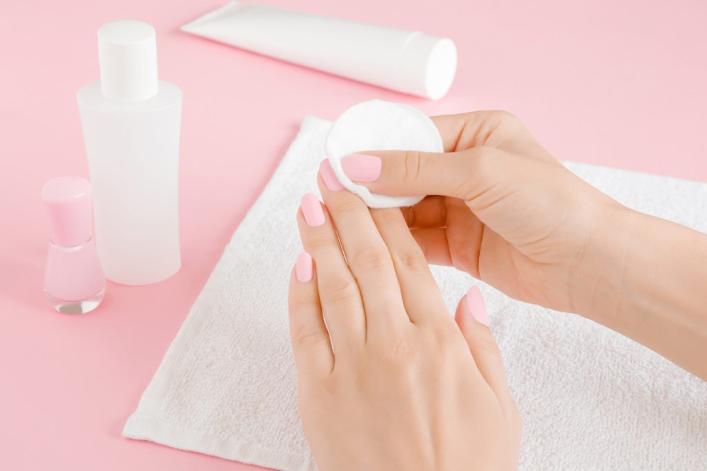 Woman's hand removing pink nail polish with white cotton pad on towel. Closeup