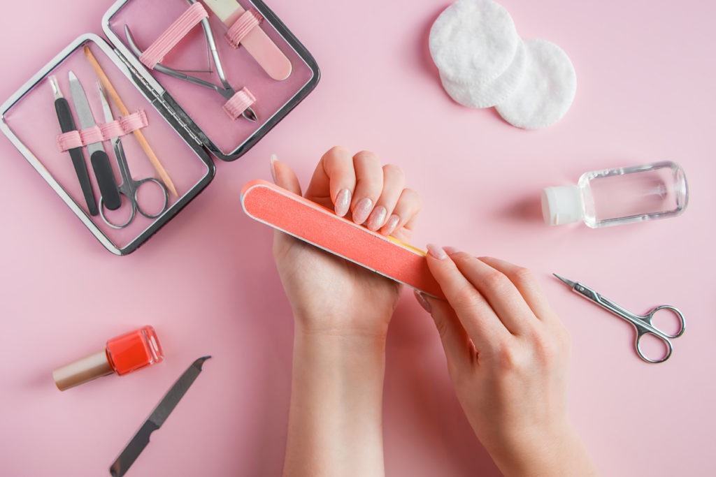 Woman’s hand holding a nail file surrounded by manicure cleaning tool set on pink background