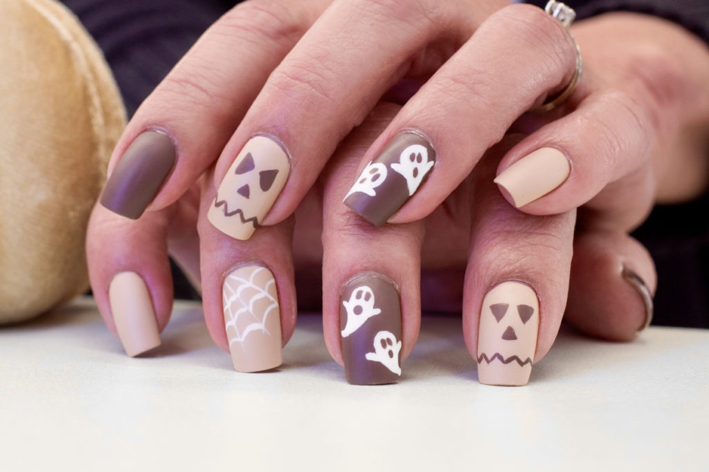 Woman’s nails designed with ghosts, spiders, and pink ribbon