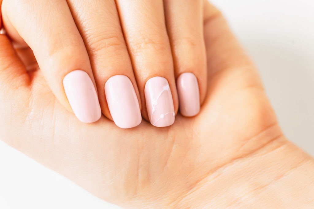  Woman’s nails with pink pastel-colored nails and a little pink ribbon accessory