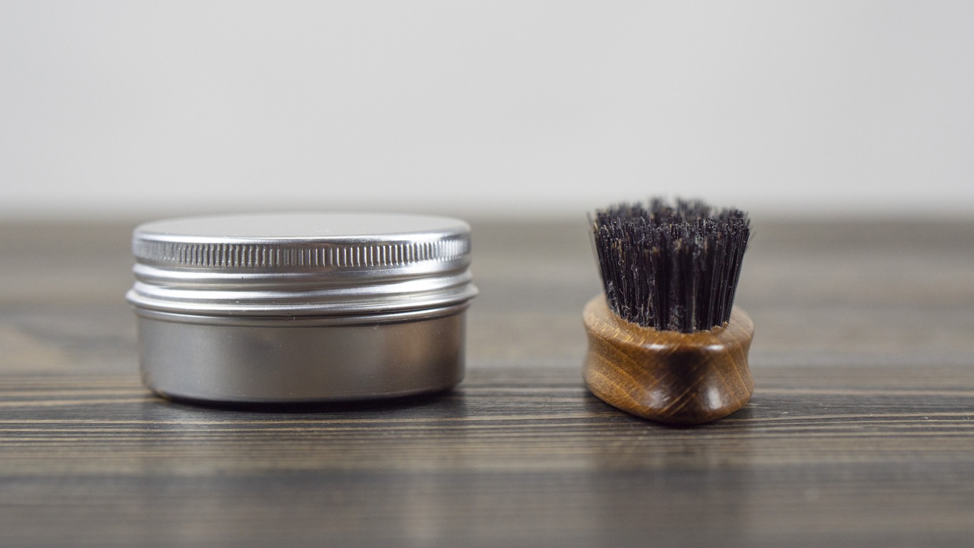 A beard brush with a mustache wax jar on a table