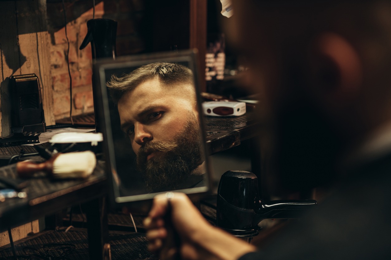 A man looking at himself after styling his hair and beard