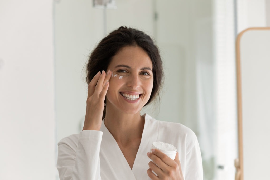 Head shot portrait overjoyed woman applying moisturizing lotion on cheek