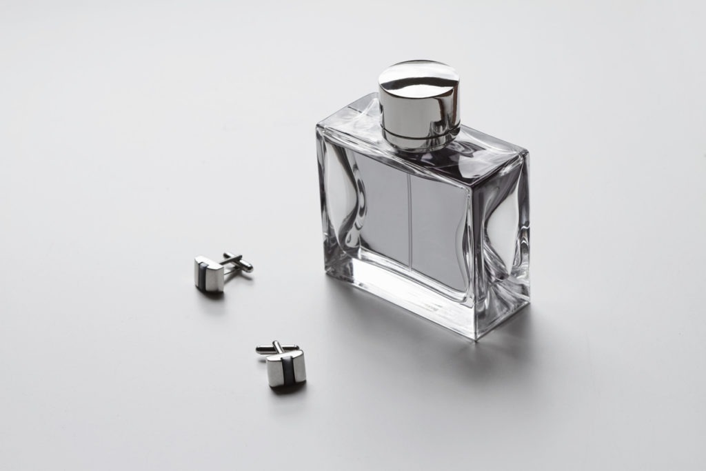 A bottle of men’s cologne with a pair of cufflinks