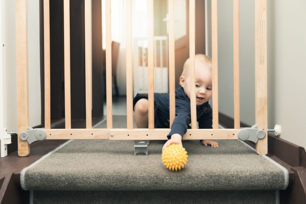 Child-playing-behind-safety-gates-in-front-of-stairs-at-home