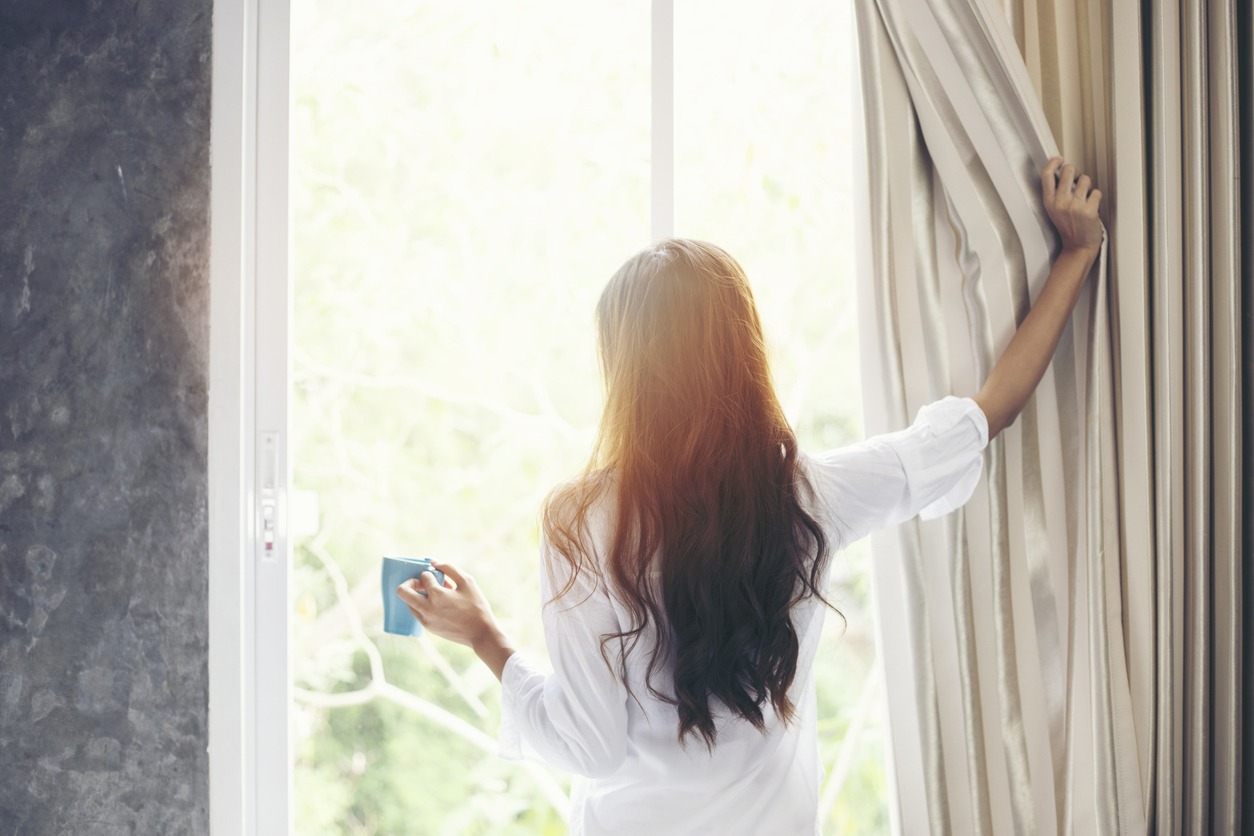 Asian women drinking coffee and wake up their bed fully rested and open curtains in the morning to get fresh air