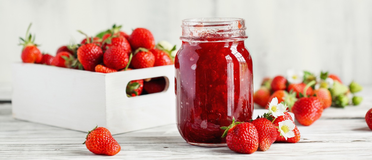 Homemade strawberry preserves or jam in a mason jar surrounded by fresh organic strawberries