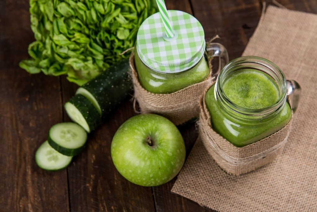 A green apple beside two glasses of blended vegetables