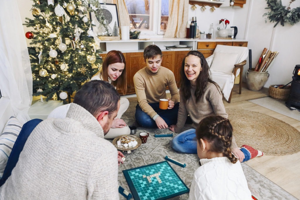 Big family sitting on the floor playing intellectual board games together while spending leisure time at home. Father, mother, grandmother, and kids play a traditional game with letter tiles