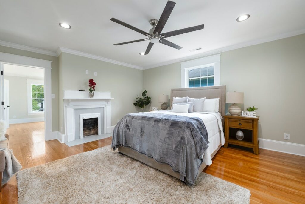 a cozy bed with ceiling fan on top