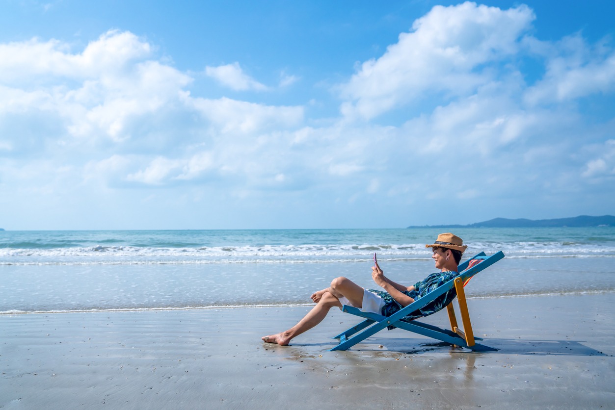 Young Asian man resting on beach chair with using smartphone
