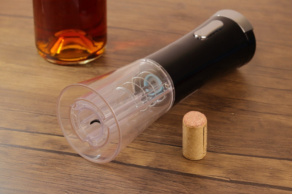 An electric corkscrew on a table with a cork from a wine bottle