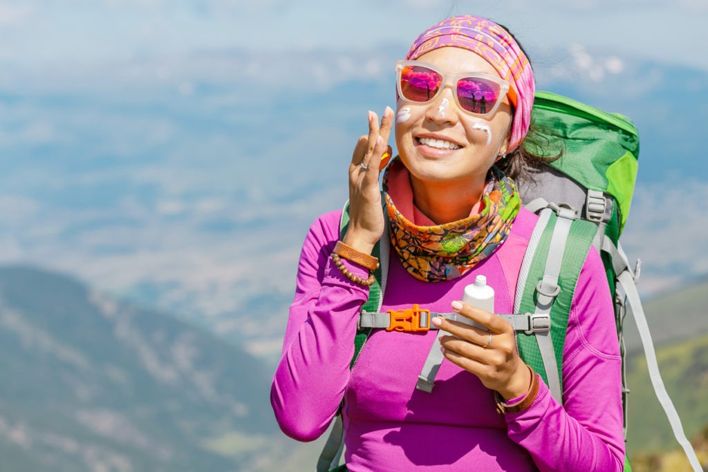 Hiker woman applying sun cream to protect her skin from dangerous uv sun rays high in mountains. Travel healthcare concept