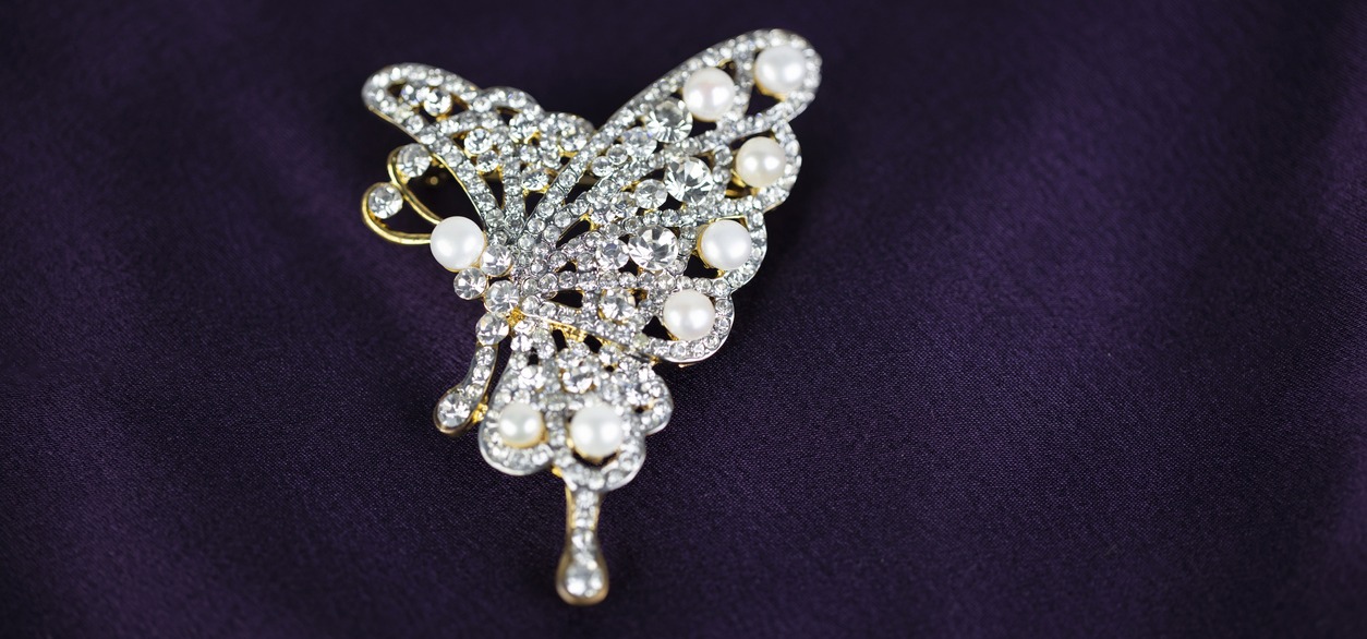 butterfly-shaped brooch with diamond and pearl accents in purple silk background