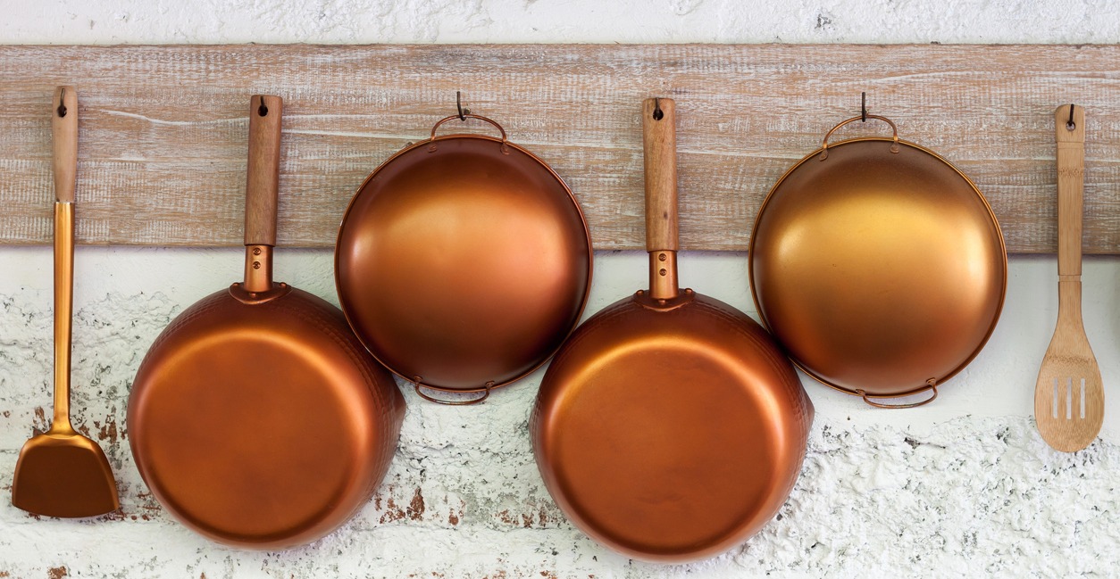 copper cookware set hanging on a white wall
