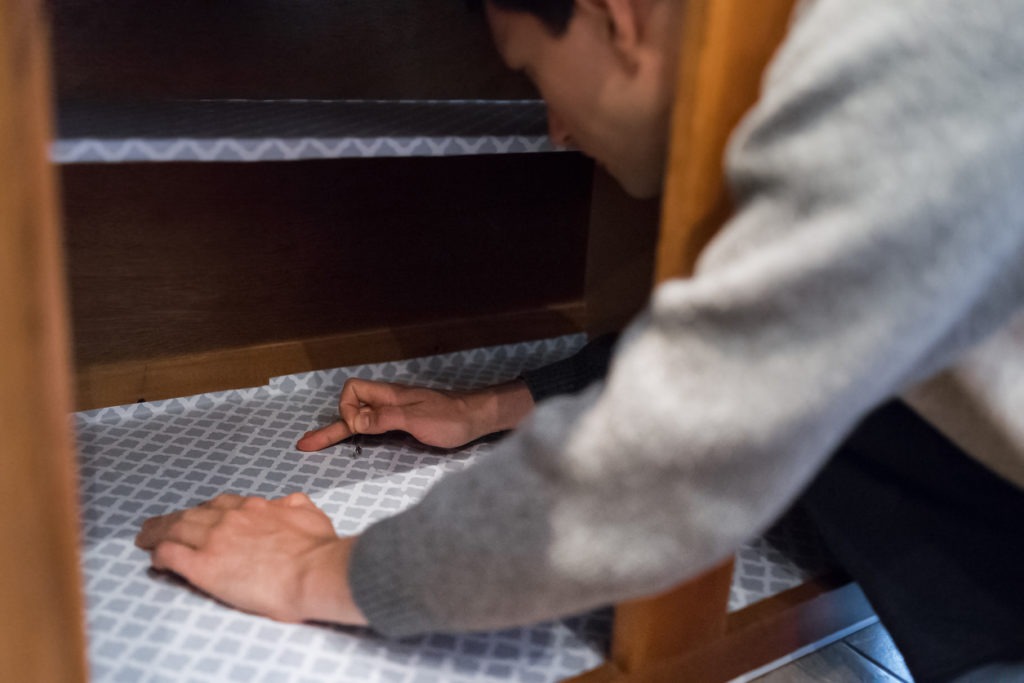 Man placing protective liner sheet inside on wooden cabinets with hands, pricking with pin in kitchen drawers