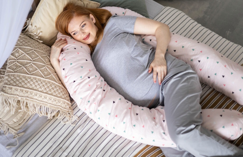 a picture of a pregnant woman lying on a bed hugging a pillow