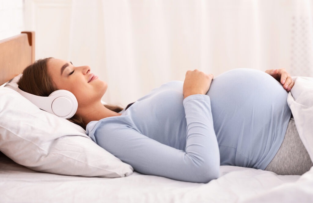 a pregnant woman lying on her bed listening to music