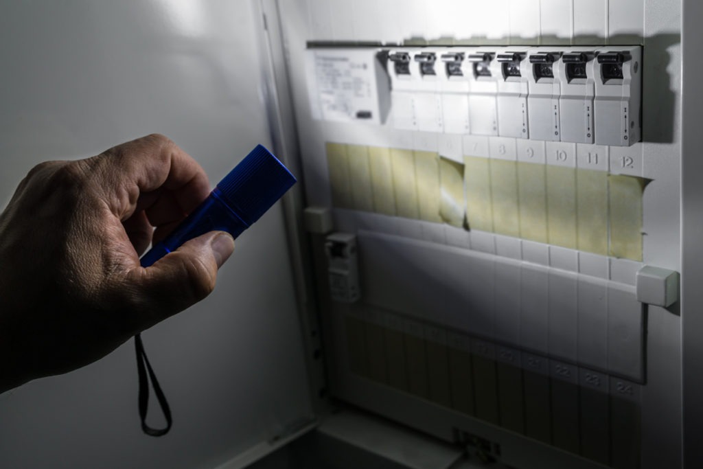 Fuse box with fuses in a distribution box during a power outage illuminated with blue flashlight held by a man, Germany