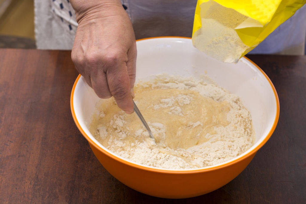 Woman-kneading-homemade-bread-with-organic-flour-in-domestic-kitchen-in-her-white-apron
