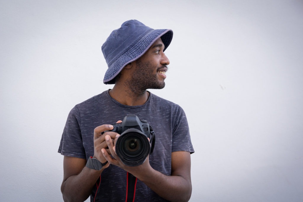 A man wearing a Kangol hat and holding a camera
