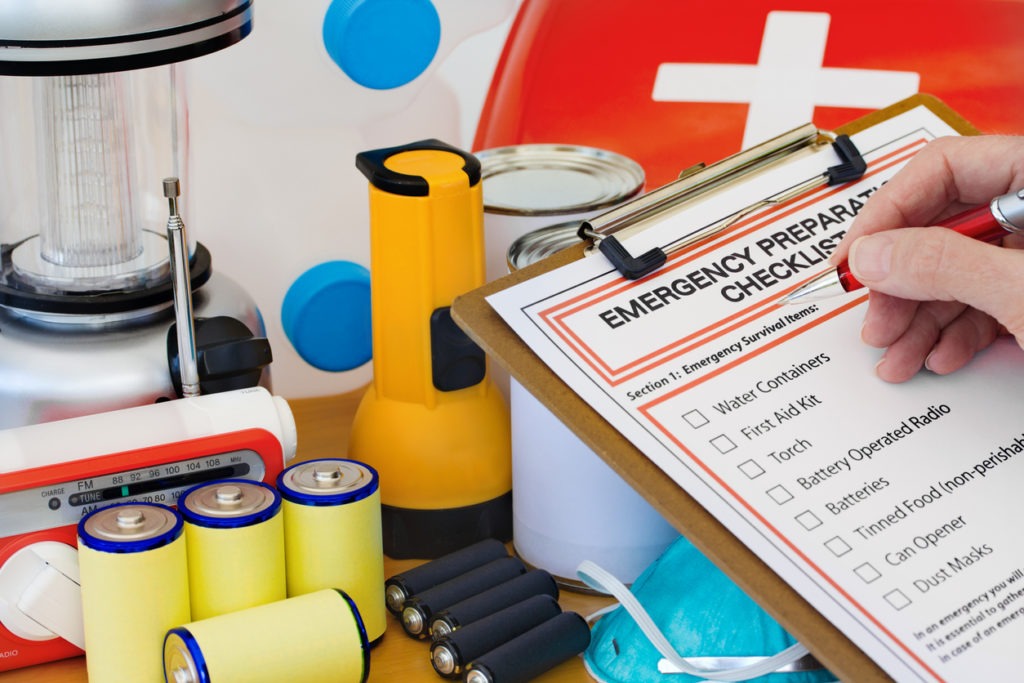 A person checking off items on the emergency preparedness checklist with supplies on the background