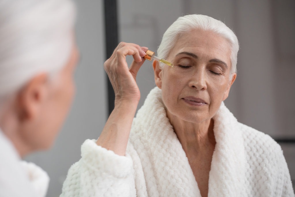 Elderly woman applying serum using a dropper to her face