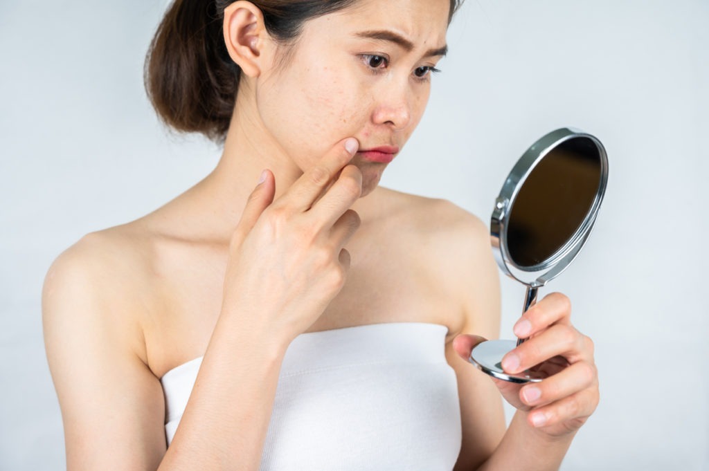 Image of a woman feeling upset about her dark circles while looking at her reflection in the mirror 