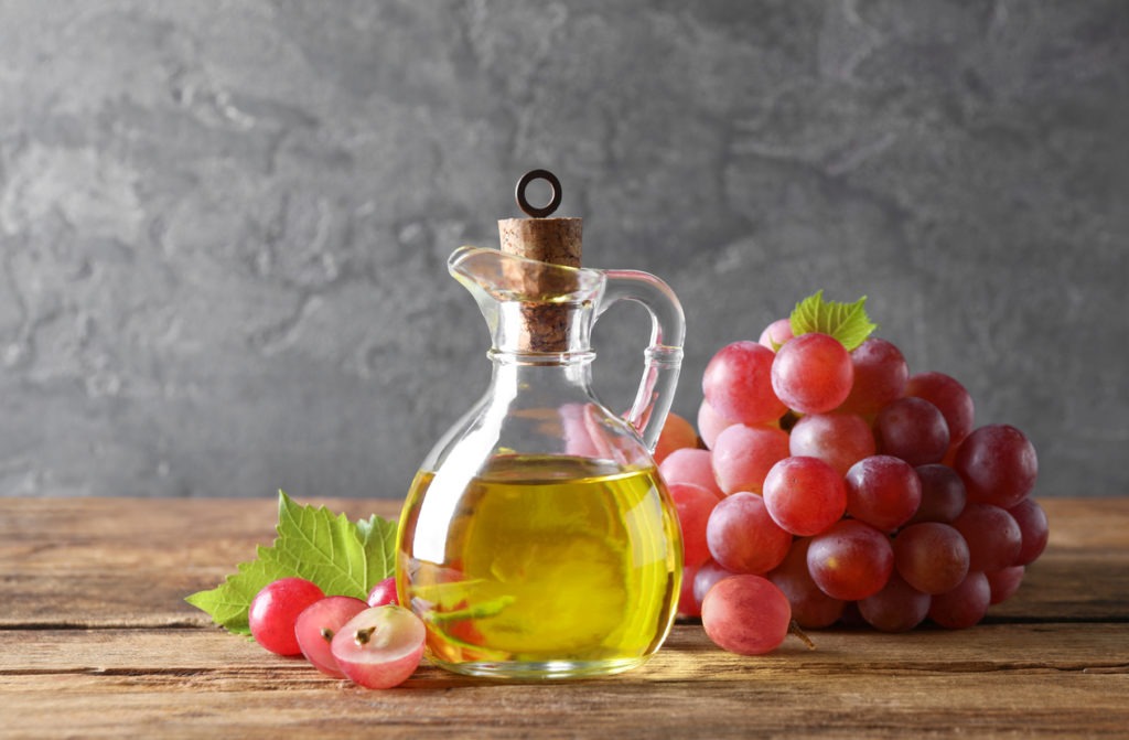 Natural grape seed oil in a jug on a wooden table. 