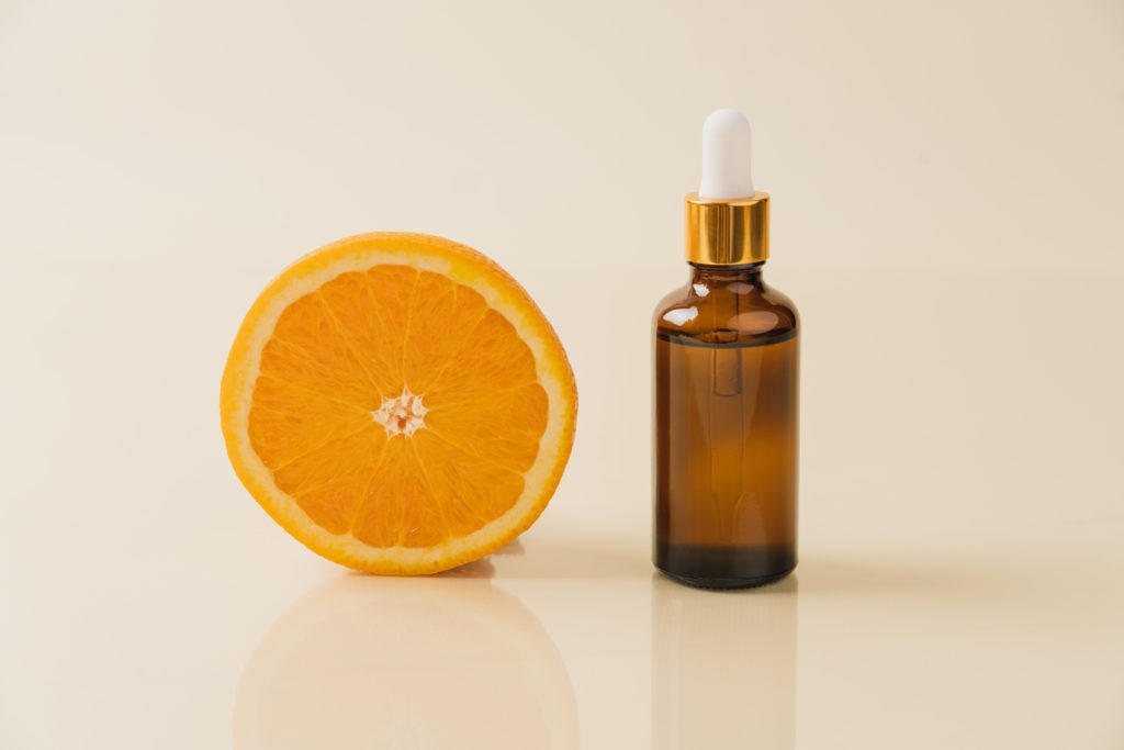 Vitamin C serum on a brown transparent bottle with a dropper beside a sliced orange