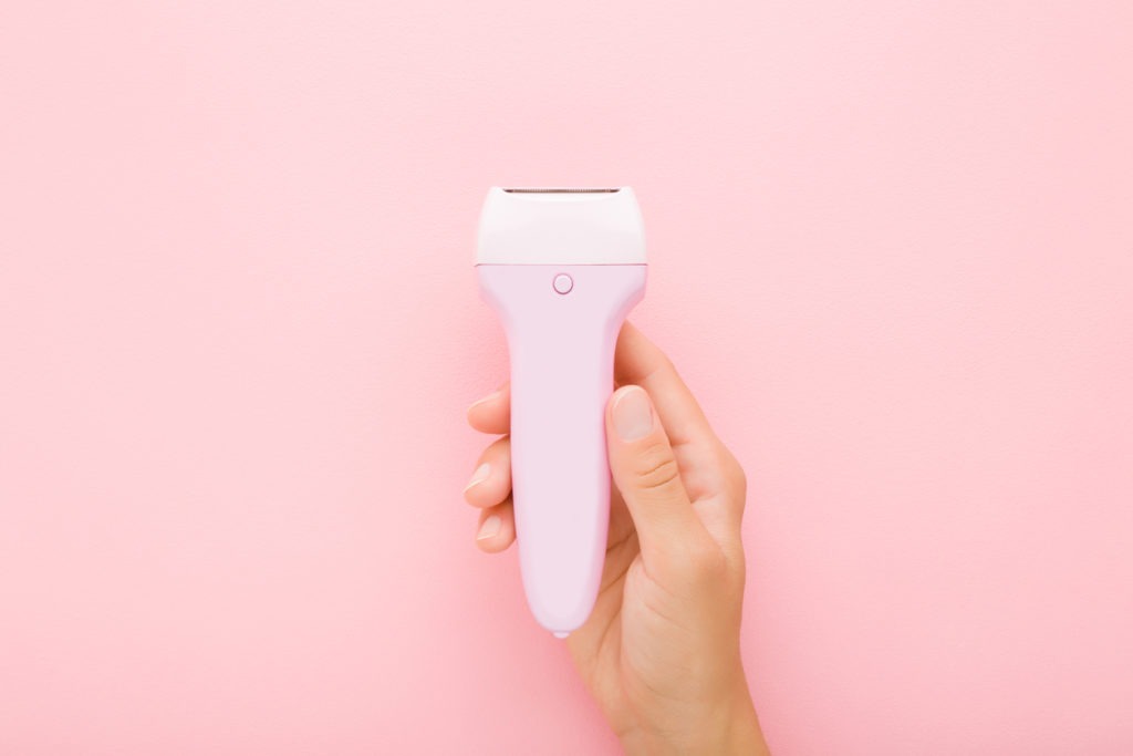 woman holding a pink electric epilator in pink background